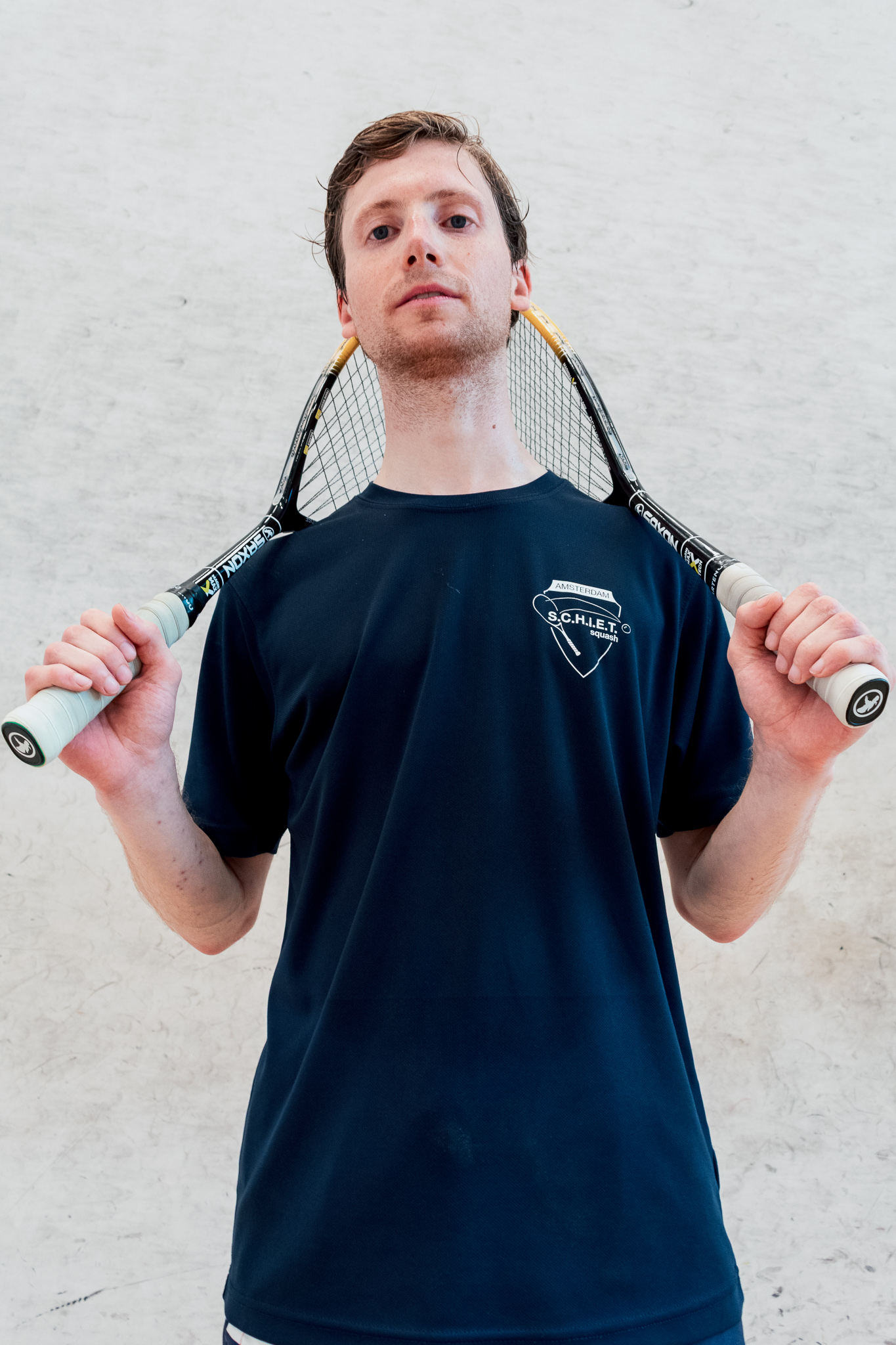 Portrait of a squash player holding two rackets over his shoulders