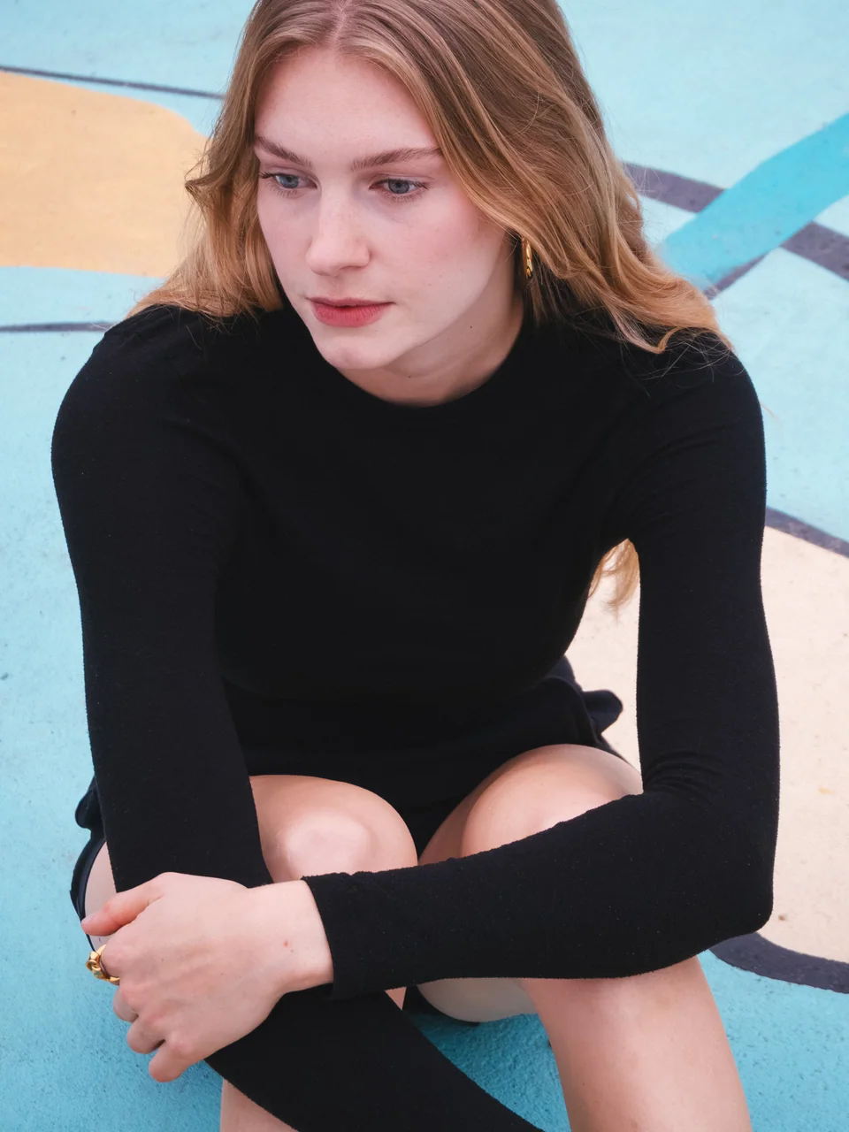 Portrait of a woman in a black dress seated against a blue wall